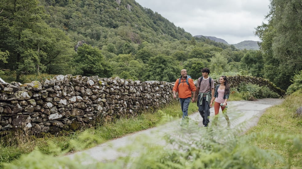 A wide angle front view of a father and his two teenage children who are out enjoying a hike together in Keswick in the Lake District in Cumbria